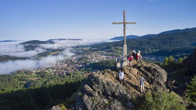 Mehrere Wanderer stehen am Gipfelkreuz des Silberbergs und blicken hinab auf Bodenmais, wo der Nebel hineinkriecht. | © Bodenmais Tourismus & Marketing GmbH