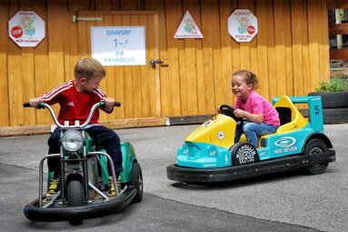 Ein Mädchen und ein Junge sitzen auf kleinen elektrischen Fahrzeugen und fahren damit um die Wette. | © Bodenmais Tourismus & Marketing GmbH