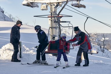 Vater und Tochter steigen aus dem Skilift aus. Ein Mitarbeiter hilft dem Mädchen dabei. | © Bodenmais Tourismus & Marketing GmbH