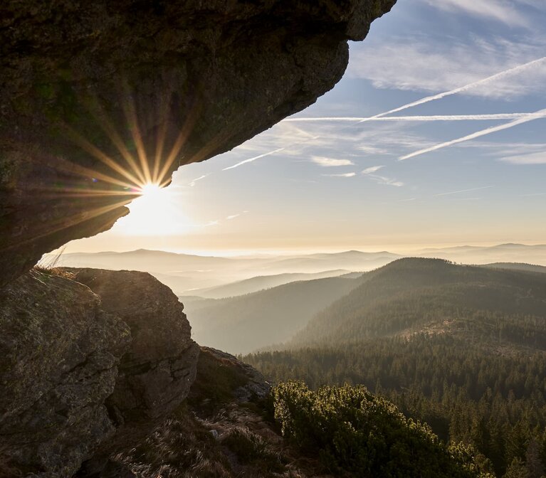 Unter einem hervorstehenden Felsvorsprung hindurch blickt man zur niedrig stehenden Sonne und Nebel im Tal. | © Bodenmais Tourismus & Marketing GmbH