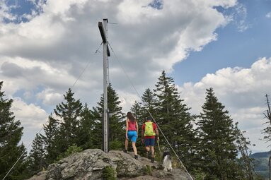Eine Frau und ein Mann gehen zusammen mit einem Hund die letzten Schritte bis zum Gipfelkreuz des Kleinen Arbers. | © Bodenmais Tourismus & Marketing GmbH