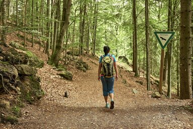 Eine Frau wandert durch den Wald und an einem Schild vorbei auf dem "Naturschutzgebiet" steht. | © Bodenmais Tourismus & Marketing GmbH