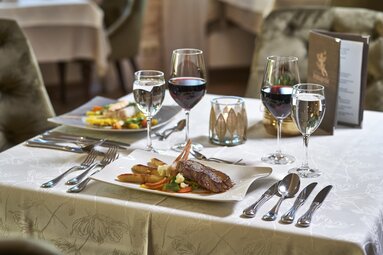 Auf einem edel gedeckten Tisch wurden Speisen und Getränke angerichtet. Auf den Tellern befindet sich ein Filetstück und Gemüse. Daneben stehen je ein Glas Rotwein und Wasser. | © Bodenmais Tourismus & Marketing GmbH