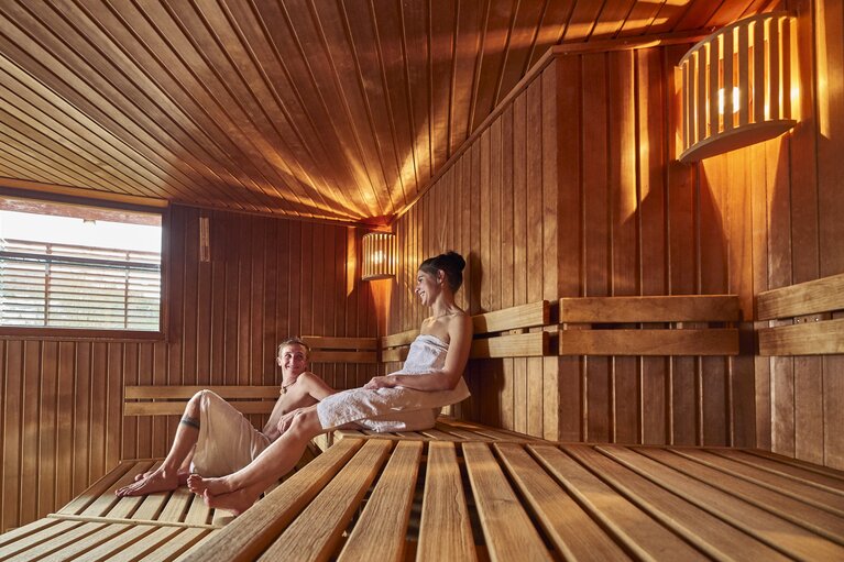 Eine Frau und ein Mann sitzen auf zwei unterschiedlichen Stufen in einer Sauna. | © Bodenmais Tourismus & Marketing GmbH