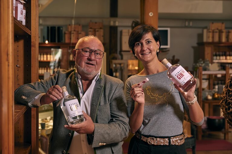 Eine Frau und ein Mann stehen in einem Verkaufsladen und halten je eine Falsche Gin in die Kamera. | © Bodenmais Tourismus & Marketing GmbH